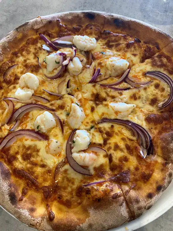 A freshly baked pizza topped with plump prawns, melted cheese, and slices of red onion on a golden, crispy crust. The pizza is served on a white plate, showcasing its vibrant and appetizing toppings.
