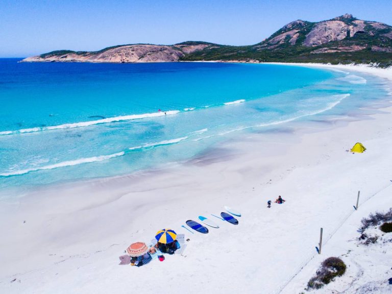 people lying on white sand beach with coliyrful sun umbrellas and the turquoise waves lapping onto the beach on a summers day with blue skies