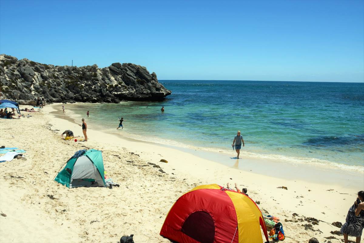 the sandy beach and turquoise ocean at little parakeet bay with people sunbathing and sun tents on the beach