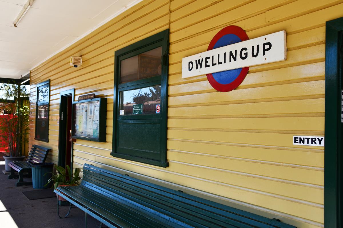 yellow weatherboard train station with a sign saying dwellingup