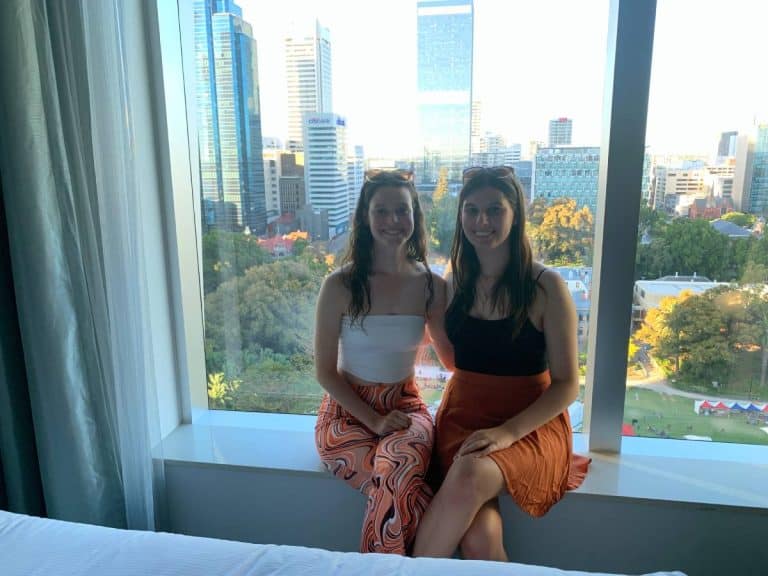 two girls sitting on a window sill in a hotel room overlooking city park