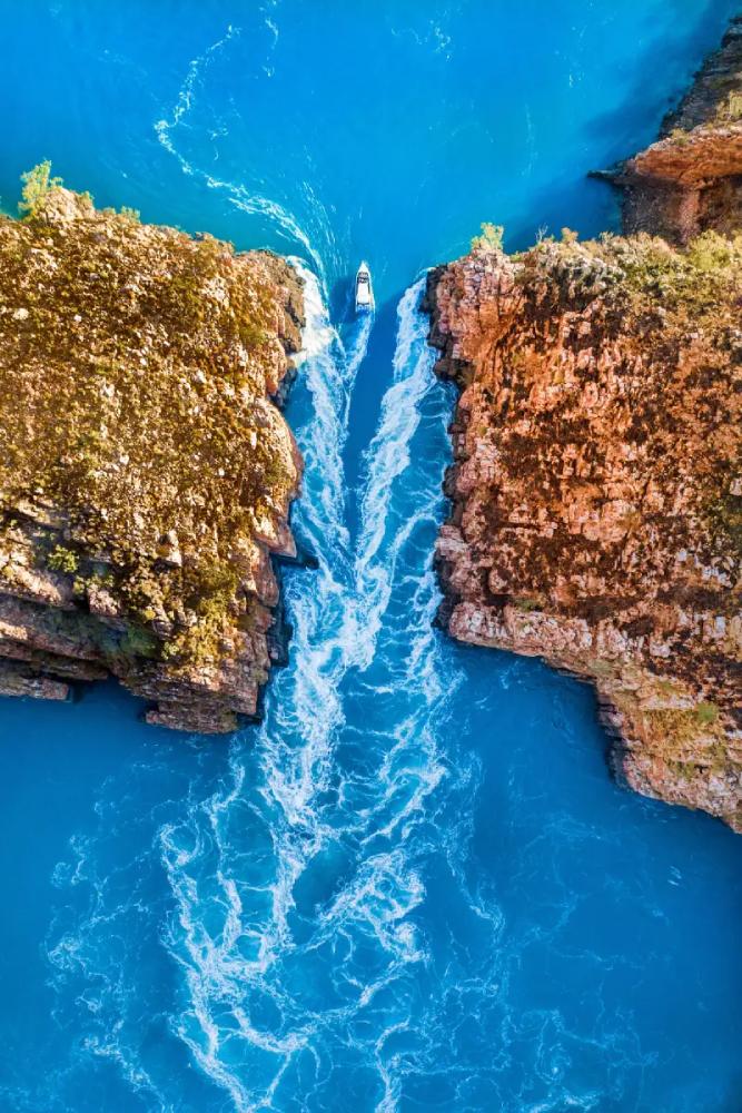 aerial view of water running horizontally through a gap in rocks