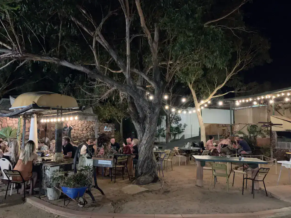 The Best Kalbarri Restaurants, Bars, and Cafes: My Guide for 2026 1 A cozy outdoor dining area under string lights and trees, with people enjoying their meals in a relaxed, dimly lit atmosphere