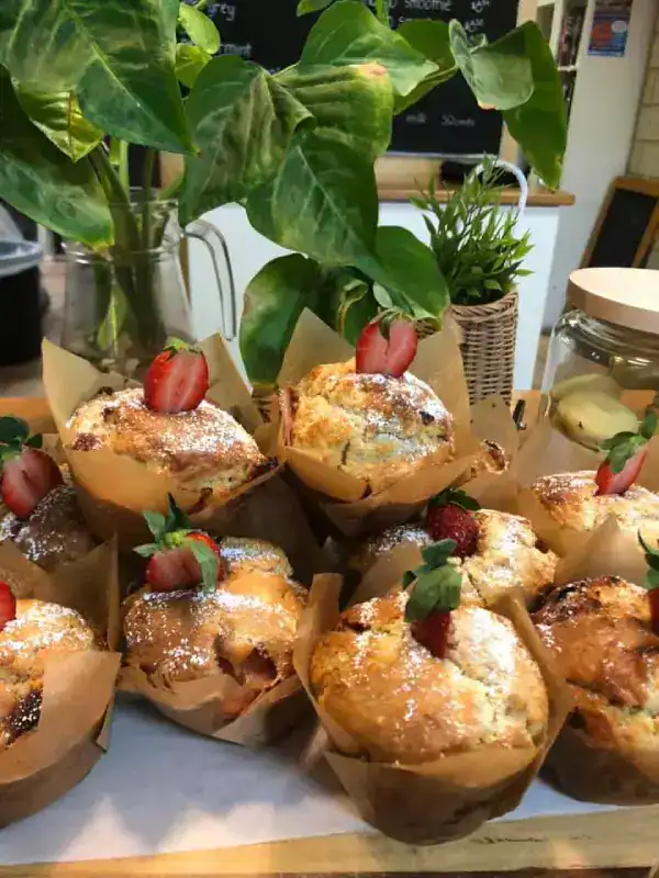The Best Kalbarri Restaurants, Bars, and Cafes: My Guide for 2026 18 Freshly baked muffins dusted with powdered sugar, each topped with a halved strawberry, placed on a counter near green potted plants.