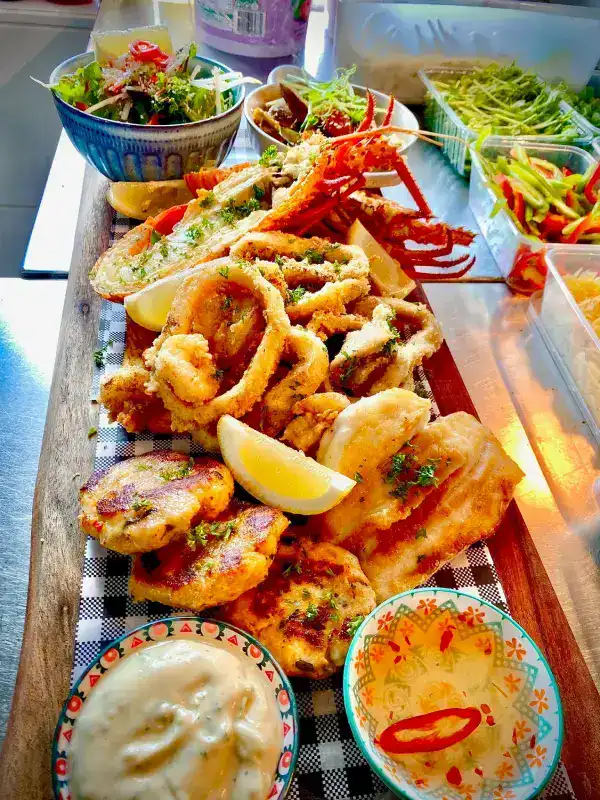 The Best Kalbarri Restaurants, Bars, and Cafes: My Guide for 2026 17 A wooden board filled with crispy fried seafood, including calamari and prawns, served with lemon wedges, dipping sauces, and a side salad