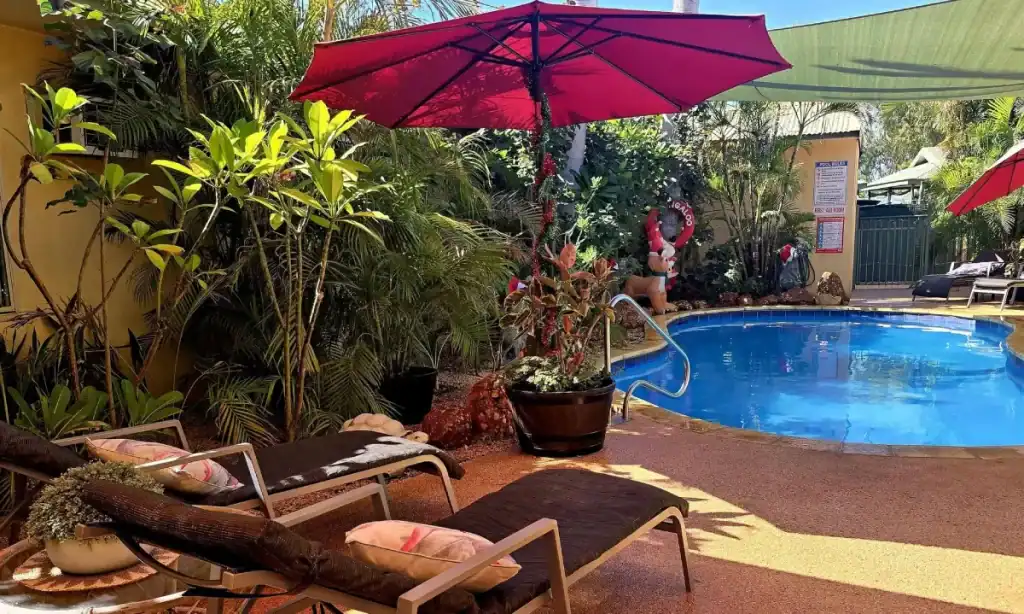 Where to Stay in Exmouth: Best Hotels & Areas 5 a tropical pool with red sun umbrella and sun loungers amongst lush gardens at ningaloo lodge exmouth